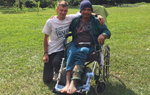 ein ADRAlive!-Freiwilliger in Bolivien, der zusammen mit einem einheimischen Menschen mit Beeinträchtigung, der auf einem Rollstuhl sitzt, zu sehen ist. Beide haben den Arm um sich.