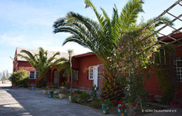 Das Gebäude der Kindertagesstätte „Nuestro Hogar“ in Peru, umrahmt von zwei schönen Palmen