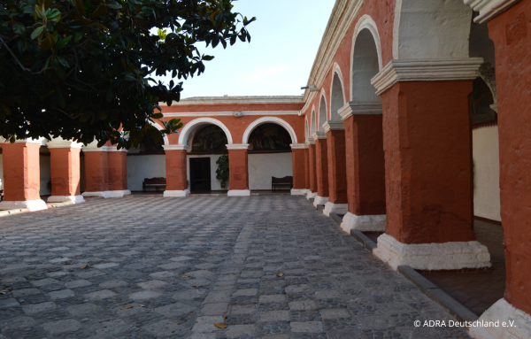 Blick auf den Innenhof der Kindertagesstätte „Nuestro Hogar“ mit rot-weiß gestrichenen Wänden und abgerundeten Säulenbereichen, die Arkaden bilden