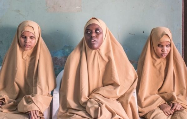 Drei Frauen mit Sehbehinderung sitzen auf Stühlen vor einer Wand