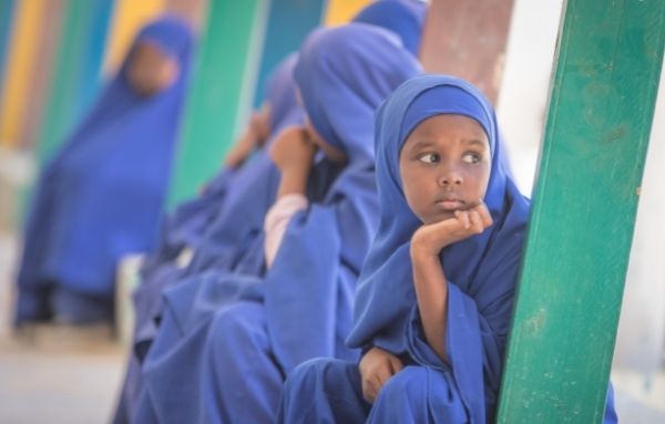 Eine Gruppe aus Schulmädchen in Schuluniform sitzt auf Bänken im Schulkorridor