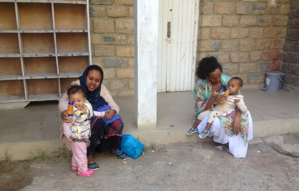 zwei Mütter sitzen vor einer Kinderklink auf einer Stufe und füttern ihre Kinder mit einem Saft