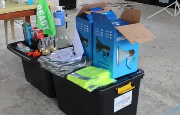 zwei schwarze Kitinhaltboxen, die ein paar Warnwesten, Megafon, Fahnen und Glocken beinhalten