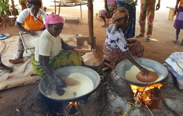 Zwei Frauen sitzen auf dem Boden und Kochen auf offenen Feuer mit großen Pfannen Hirse