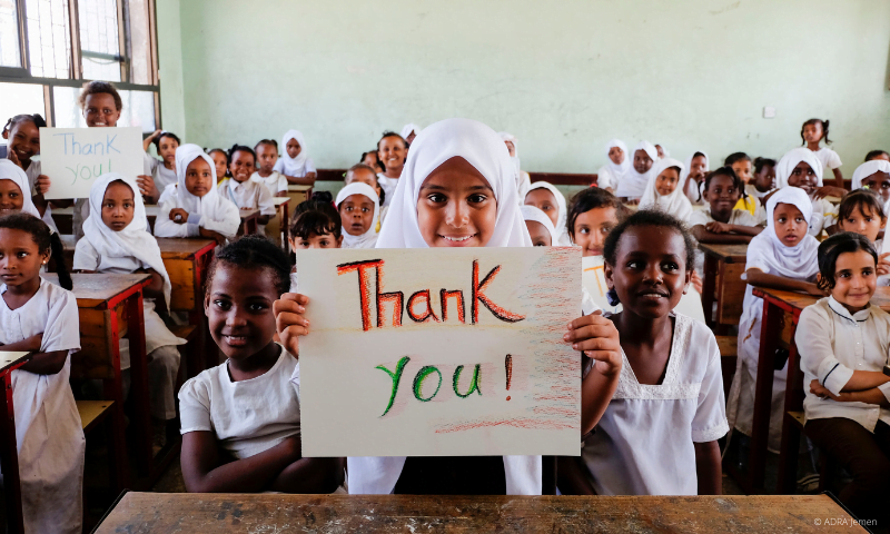 Eine Schulklasse blickt lächelnd in die Kamera und hält ein "Thank you" Schild nach oben