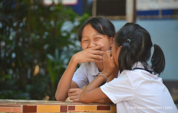 Fröhliche Schulmädchen in Thailand lachen herzhaft auf einer Pausenhofbank