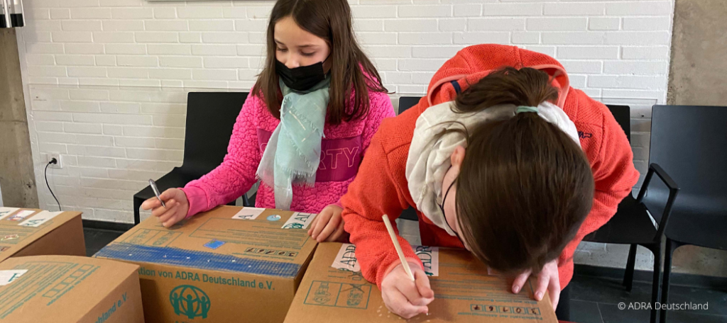 Zwei Mädchen packen und beschriften Pakete für die Aktion Kinder-helfen-Kindern