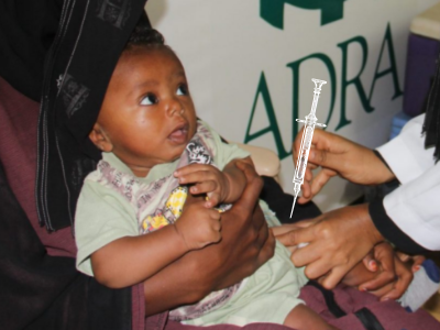 Ein Kleinkind bekommt eine Impfung von einer Ärztin auf dem Oberschenkel, während es auf dem Schoß der Mutter sitzt