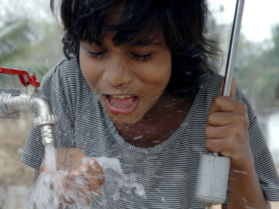 Ein Kind hält die Hand unter einem laufenden Wasserhahn, um Wasser zu trinken