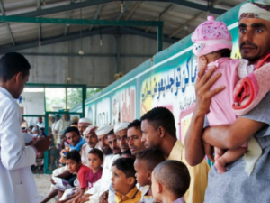 Männer sitzen im Wartebereich einer Kinderklink mit ihren Kindern auf dem Schoß, während einer der Männer daneben steht und sein Kind im Arm hält