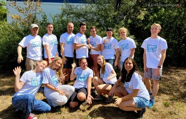 15 junge Erwachsene stehen lachend im Freien, alle tragen ADRA live!-T-Shirts. | © ADRA Deutschland e. V.