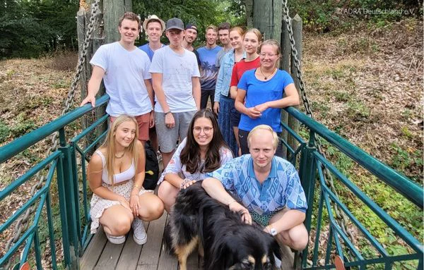Eine Gruppe von Freiwilligen steht auf einer Brücke, lächelt in die Kamera – ein Hund sitzt vorn. | © ADRA Deutschland e. V.