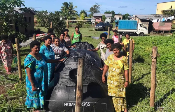 Eine Gruppe von Frauen stehen um das Biogas herum und schauen in die Kamera