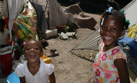 Zwei junge Mädchen haben Spaß und lachen. Im Hintergrund sind Zelte und Bettlacken aufgestellt