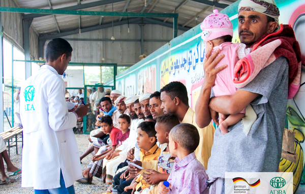 Ein Arzt steht vor einer Gruppe von Männern und Kindern im Wartebereich der Klinik im Jemen.