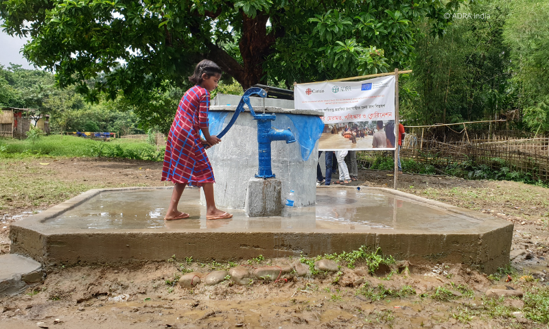 Ein junges Mädchen aus Indien steht vor einer Wasseraufbereitungsanlage und zapft sich sauberes Trinkwasser in eine Plastikflasche.