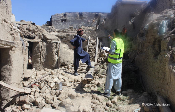 Zwei Männer stehen inmitten der hinterlassenen Ruinen eines Erdbebens in Afghanistan.