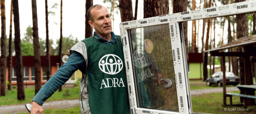 Ein ADRA- Mitarbeiter in grüner ADRA-Weste trägt ein neues Fenster