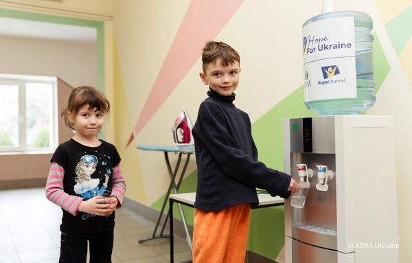 Kinder betätigen Wasserspender in der Ukraine-Winterhilfe