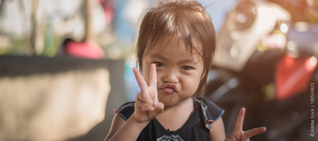 Kleines Mädchen macht einen Kussmund und zeigt mit beiden Händen das Peace-Zeichen