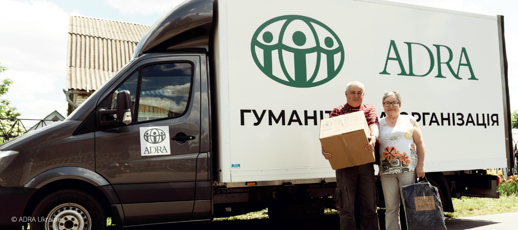Ein Mann und eine Frau stehen vor einem ADRA-LKW in der Ukraine, welcher Hilfspakete an die Betroffenen aushändigt.