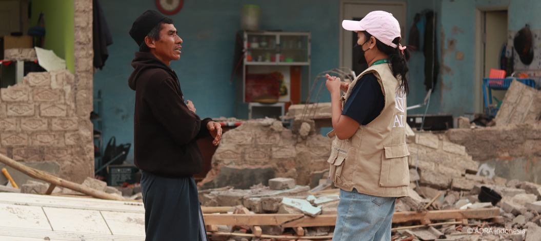 Eine ADRA-Mitarbeiterin aus Indonesien steht mit einem vom erdbebenbetroffenen Bewohner vor den Trümmern eines Hauses