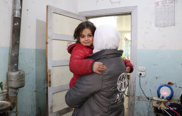 Eine ADRA Mitarbeiterin aus Syrien hält ein junges Mädchen im Arm