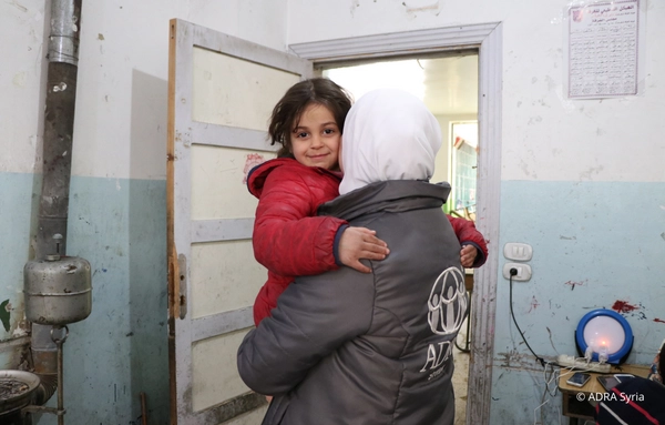 Eine ADRA Mitarbeiterin aus Syrien hält ein junges Mädchen im Arm