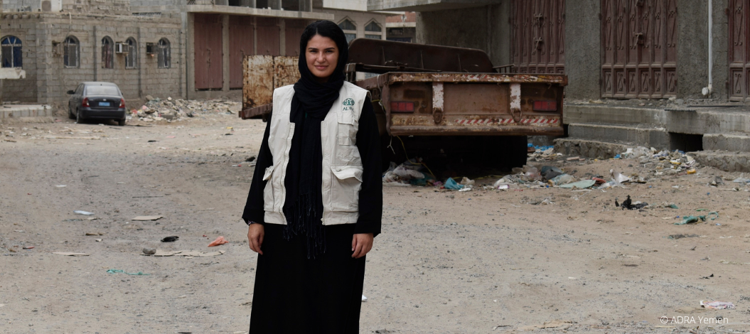 Bürgerkrieg im Jemen: Eine ADRA Mitarbeiterin steht vor den zerstörten Gebäuden, Autos und hinterlassenen Trümmern.