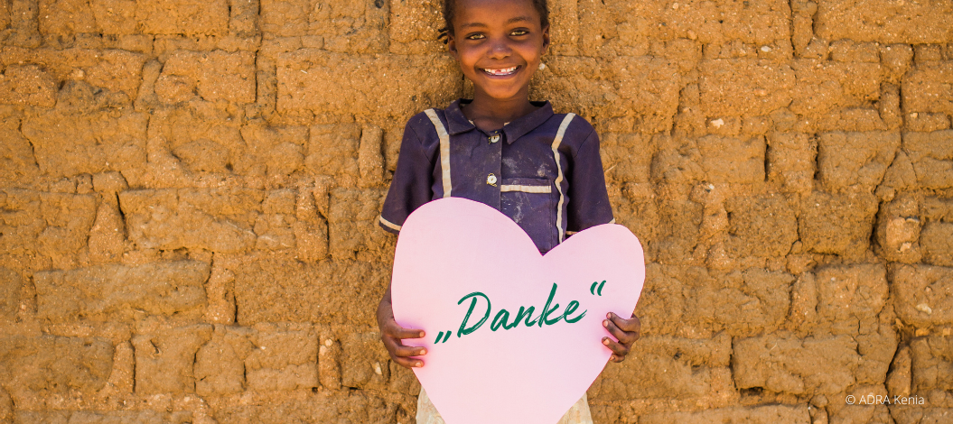 Mädchen aus Kenia hält rosa Papierherz mit schrägem „Danke“-Schriftzug