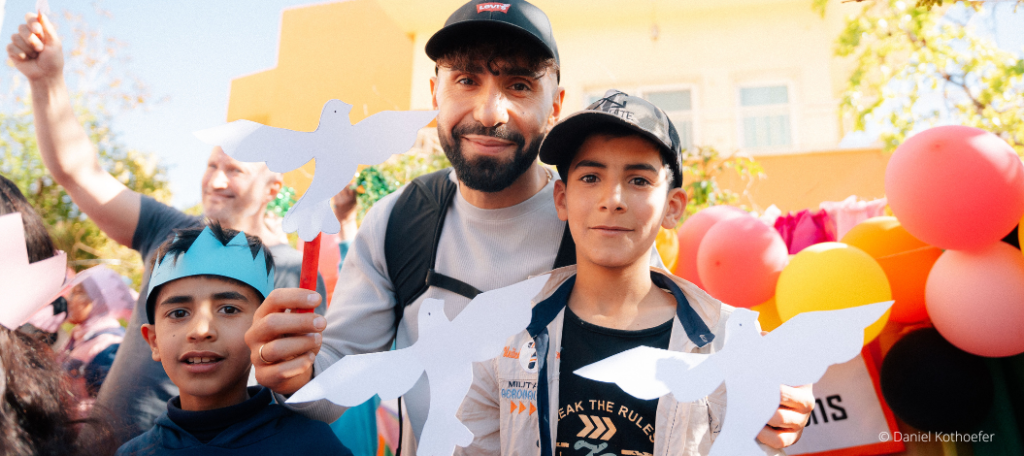 Rapper MoTrip steht im Schulhof einer Schule im Libanon mit Kindern und halten gemeinsam weißen Papiertauben in den Händen.