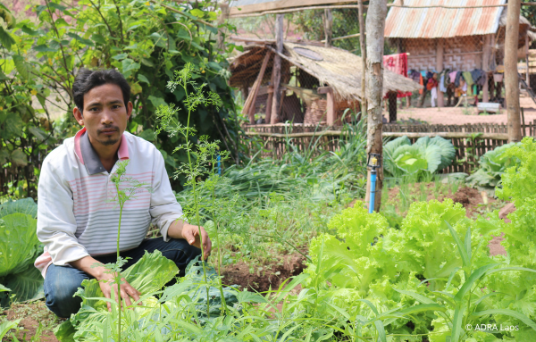 Ein Bauer aus Laos sitzt in der Hocke hinter seiner reichhaltigen Ernte