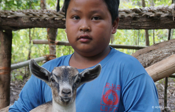Ein Kind aus Laos hält liebevoll eine Ziege im Arm, während es in die Kamera schaut