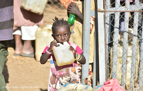 Ein kleines Mädchen aus dem Sudan trinkt aus einem Wasserkanister, den sie mit beiden Händen festhält, um ihren Durst zu stillen.