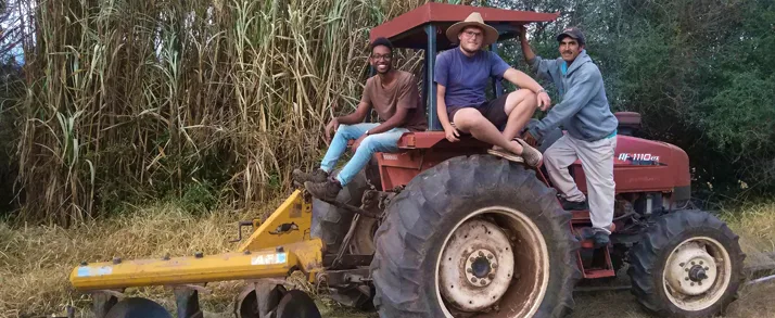Dominik sitzt mit zwei Einheimischen auf einem Traktor in Bolivien.