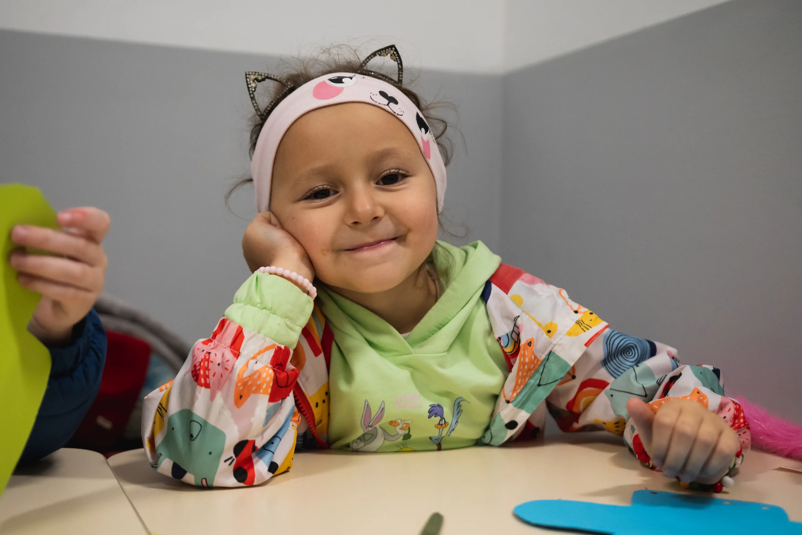 Schule "Lebendiges Wort" in Lwiw, Ukraine - Mädchen mit Katzenohren-Stirnband lächelt an einem Tisch sitzend in die Kamera