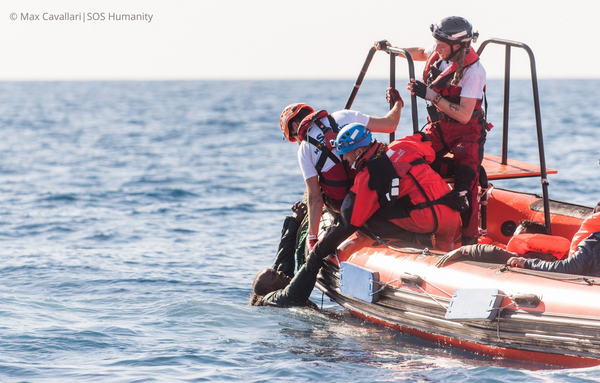 drei Helfer von SOS Humanity retten eine Person im Meer und helfen ihm, auf das Boot zu gelangen.