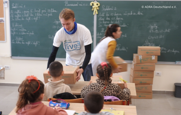 Ein Freiwilliger verteilt zusammen mit einer anderen Freiwilligen Pakete von der 'Aktion Kinder helfen Kindern!' in einer Schule in Albanien während seines Freiwilligen Sozialen Jahres (FSJ).