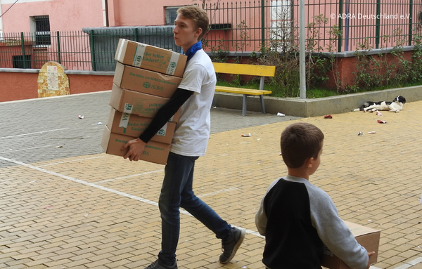 Ein Freiwilliger trägt fünf Pakete der 'Aktion Kinder helfen Kindern!' während seines Freiwilligen Sozialen Jahres (FSJ) in Albanien zur Verteilung.