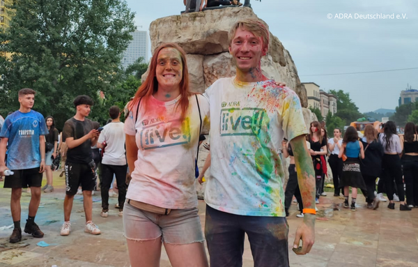 Zwei Freiwillige in bunten, mit Farbe besprühten weißen ADRAlive!-T-Shirts nehmen am Holy Color Festival während ihres Freiwilligen Sozialen Jahres (FSJ) in Albanien teil