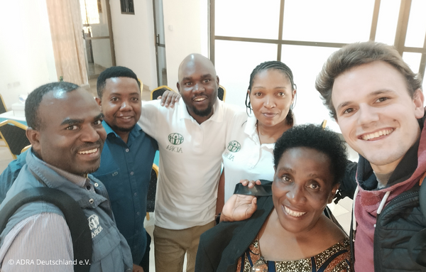 Ein ADRAlive!-Freiwilliger befindet sich mit Mitarbeitern im ADRA Tansania Büro und sie lachen fröhlich in die Kamera