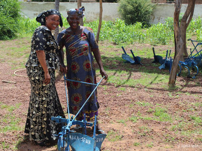 Zwei Frauen aus Mali arbeiten auf einem Feld mit einem Handpflug. Das Bild bewirbt ein Produkt im ADRA-Spendenshop: Ein Pflug für Landwirtinnen.