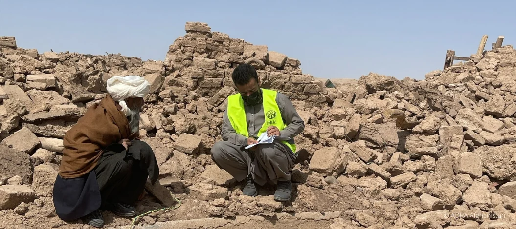 Erdbeben Herat 2023: Ein ADRA-Mitarbeiter sitzt einfühlsam mit einem betroffenen Mann auf den Trümmern, zeigt Mitgefühl und steht bereit, Unterstützung in der akuten Notlage Afghanistans zu bieten.