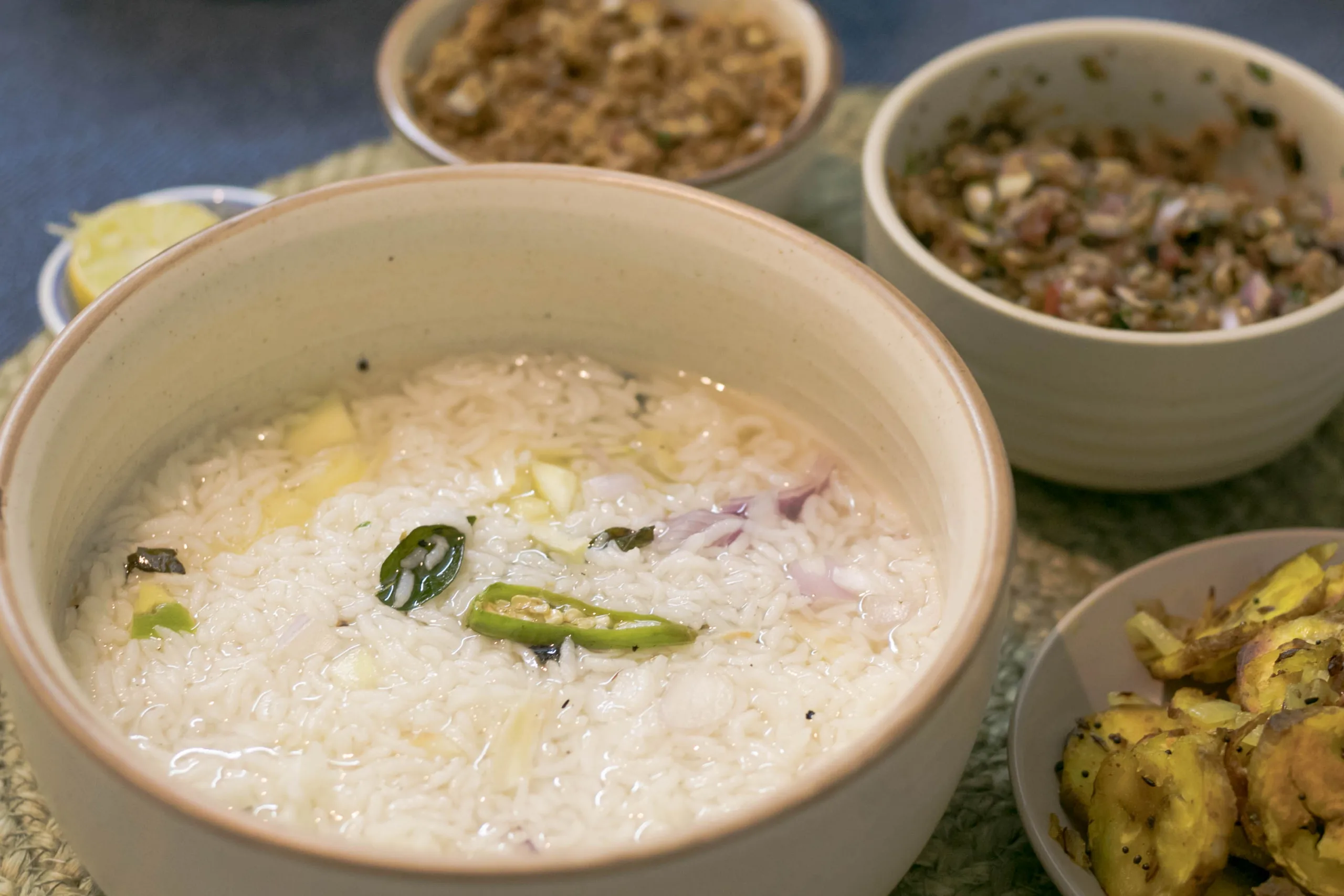 Schüssel mit Reissuppe, garniert mit Zwiebeln und grünen Chilischoten, dazu verschiedene Beilagen