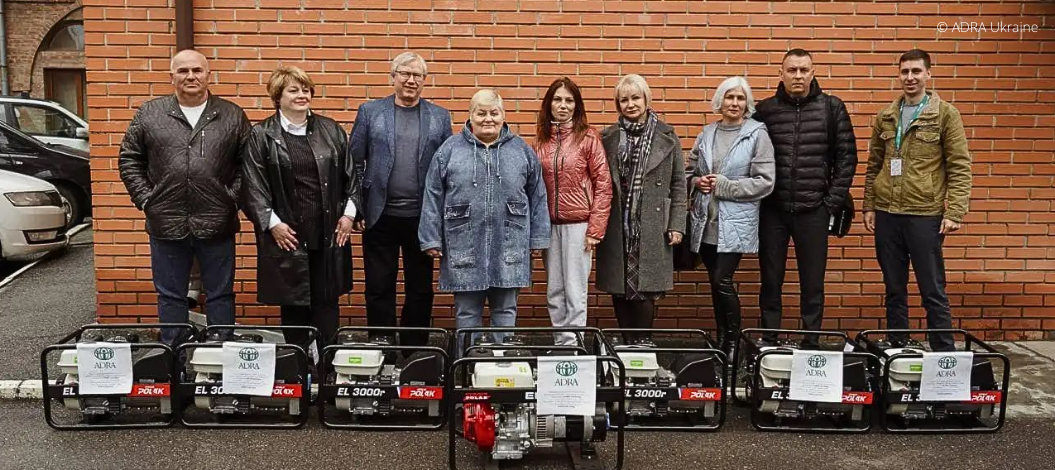 Gruppe von Menschen steht hinter sieben Stromgeneratoren, Symbol für Spendenhilfe in der Ukraine