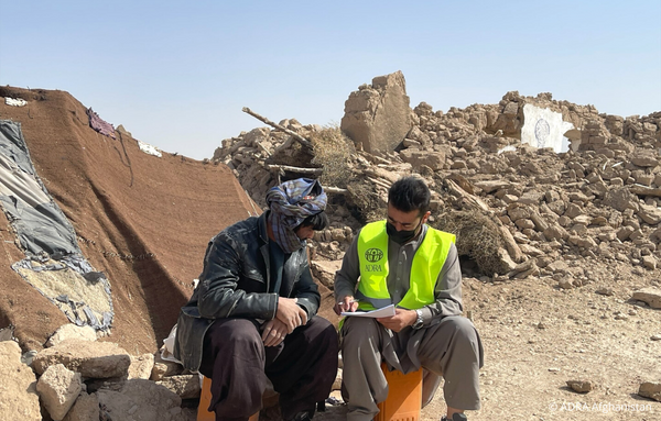 Nach dem Erdbeben in Herat, Afghanistan: Ein erdbebenbetroffener Mann betrachtet die zerstörte Landschaft, während ein mitfühlender ADRA-Mitarbeiter Hilfe leistet