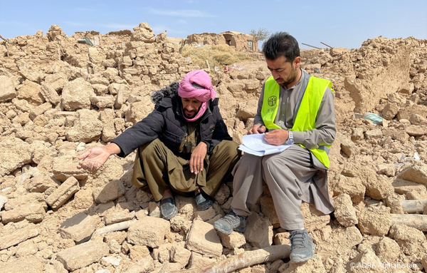 Nach dem Erdbeben in Herat, Afghanistan: Ein erdbebenbetroffener Mann zeigt auf die Trümmer, während ein mitfühlender ADRA-Mitarbeiter Hilfe leistet
