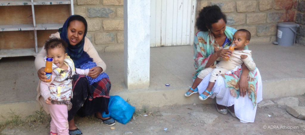 Zwei Mütter, eine gesunde Bindung: Frauen sitzen auf Treppe und geben liebevoll ihren Kleinkindern Saft. Ein Bild von Fürsorglichkeit und Gesundheit in der Schwangerschaft.