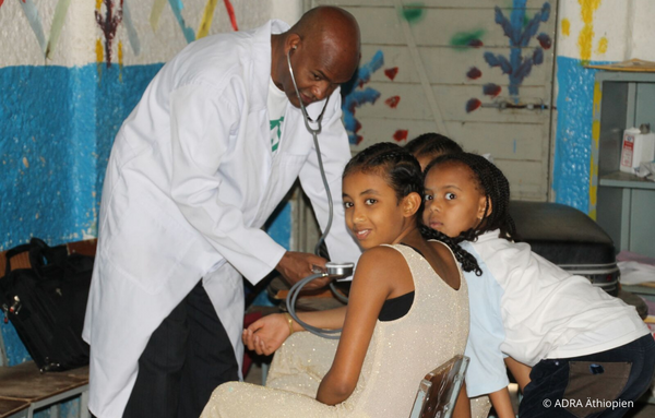 Dr. Tesfalem im weißen Kittel hört liebevoll drei kleine Mädchen mit einem Stethoskop ab. Ein Bild von fürsorglicher medizinischer Betreuung für die Gesundheit der Kleinsten in der Mekele Klinik
