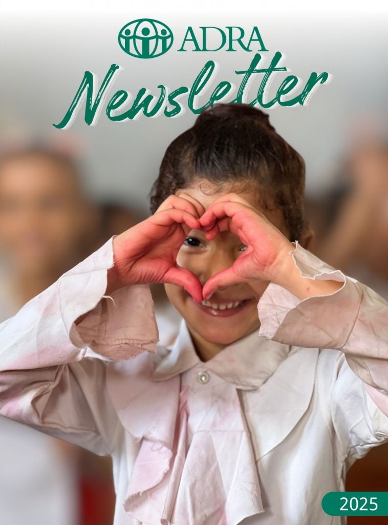 Frau erhält Hilfsgüter von ADRA-Mitarbeiter. Im Vordergrund ADRA-Logo „Newsletter 2023“. Dahinter warten weitere Personen, darunter eine Mutter mit Kind.